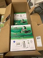 Open shipping carton showing four Titan Controls CO₂ regulator boxes inside, green and white packaging.