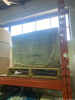 Shrink-wrapped boxed Frigidaire air conditioner on wooden pallet on metal storage shelf