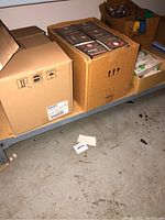 Three cardboard boxes on metal shelving containing Philips Master GreenPower cartons, Sunmaster Red Sunrise boxes, and Philips Ceramalux boxes
