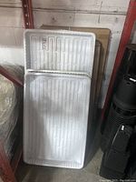 Two white plastic hydroponic trays stacked against wall