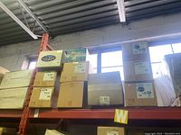 Multiple stacked cardboard boxes on warehouse shelving, labels include Can-Fan, AXC-C series and other boxed components