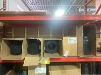 Three open cardboard boxes containing stacks of circular black plastic mesh baskets with radial openings