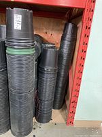 Multiple stacks of black plastic pots on shelving, showing overall lot quantity.