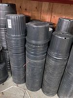 Multiple tall stacks of black plastic planter pots stacked under a shelf