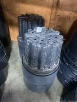 Stack of large black plastic planters with geometric patterned bottoms and drainage holes