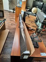 Long black corrugated cardboard box labeled “X72R Self Lock Screen” on wooden table next to tools and boxes