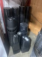 Stacks of round and rectangular black plastic plant pots against warehouse wall