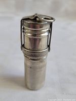 Front view of cylindrical silver-colored metal match safe with hinged top, closed with visible keyring loop on lid.