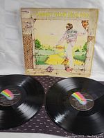 Photo showing original album cover of Goodbye Yellow Brick Road with both vinyl records partially removed from sleeve, showing MCA Records rainbow labels.