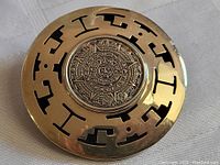 Full view of the round pendant showing the Aztec calendar motif and the outer frame with cut-out shapes.