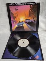 Neil Young Trans album cover with two classic cars and a man at sunset, vinyl partially visible inside sleeve.