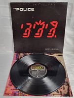 Front view of The Police Ghost in The Machine album sleeve partially open showing black vinyl record inside with center label details.