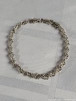 Full view of the sterling silver thick linked bracelet laid flat on a textured fabric surface.