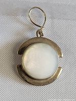 Close-up photo of the front side of the pendant showing the round mother of pearl centerpiece and the sterling silver frame with the loop attachment.