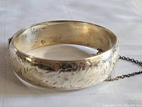 Wide sterling silver hinged bracelet with detailed floral engravings and safety chain, showing outer side closeup.