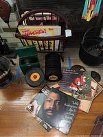 Photo showing wooden magazine rack with vinyl records inside, visible album cover for Teddy Pendergrass, and a stack of 45 RPM records nearby.