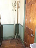 Full view of the coat rack standing beside a wall and door, showing its height and overall structure.