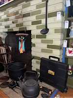 Overview photo showing cast iron cauldrons, tea kettle, wind chime hanging, iron spoon, and portable cart case near fireplace.