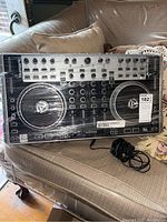 Numark N4 DJ controller front view showing jog wheels, knobs, faders, and buttons on a beige couch.