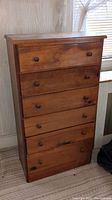 Front view of 5-drawer wooden dresser showing natural wood grain, knob-style pulls, visible knot holes and stains.