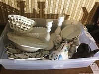 View of all milk glass bowls, plates, candle holders, ceramic dog bank, bunny figurines in plastic bin