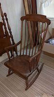 Front angled view of wooden rocking chair showing seat, armrests, and backrest slats with visible wood grain and cracks.