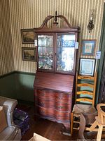 Front view of vintage wooden secretary desk with curio cabinet filled with glass figurines and items inside. Shows entire piece and surrounding room.