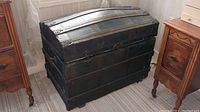 Front view of large black dome-top wooden trunk with metal straps and hardware, showing worn condition.