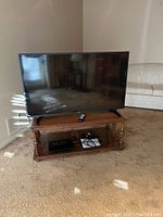 RCA 48-inch LED TV on wooden stand with Sony DVD player remote on the shelf.