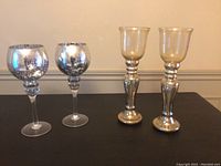 Four mercury glass candleholders grouped, two goblet-shaped and two globe-shaped, all with silver mercury finish, about 14 inches tall.