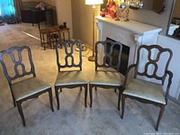 Four wooden chairs arranged on carpet, three side chairs and one arm chair with light upholstery seat covering.