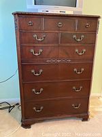 Front view of mahogany-tone tall chest with nine drawers and brass-tone handles.
