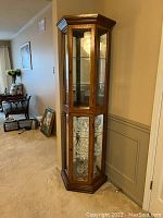 Full view of the curio cabinet in a room corner, showing wood frame and glass shelves inside with some glassware removed.
