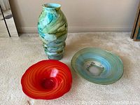 Three-piece decorative glassware set including a tall vase with green and blue marbling, a greenish-blue swirl bowl, and a red bowl with concentric ring texture.