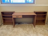 Photo showing a wood desk positioned between two matching wood bookshelves on carpet near a window.
