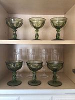 View of six green glass dessert dishes and four clear glass footed glasses arranged on shelves.