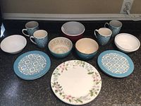 Photo showing the full lot of Corelle dishware including mugs, bowls, small plates with blue tile pattern, and a large floral dinner plate.