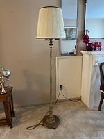 Floor lamp unlit showing pleated cream shade and ornate metal base with detailed pole design.