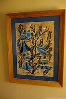 Framed artwork showing full view of four blue stylized birds perched on floral branches with blue matte and wooden frame