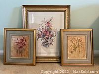Three framed floral prints displayed together showing gold-tone frames and floral artwork.