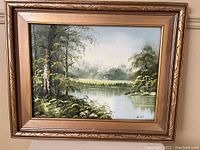 Front view of framed landscape painting by Scott depicting river, trees, and sky.