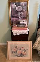 View of two framed floral art prints and a pink floral decorative box on a small table with lace cloth.