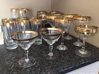 Photo showing the complete set of various glassware and stemware with gold trim arranged on a counter.