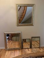 Four silver-framed rectangular mirrors displayed against a wall and on the floor. Frames have textured or patterned silver finish, varied sizes.