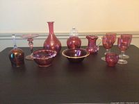 Full view of all ten ruby glass items arranged on a surface showing their shapes and colors