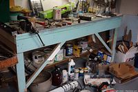 Photo of workbench with various tools, hand tools, and accessories scattered and some containers below the bench