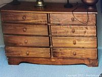 Front-facing view of the wood chest showing all nine drawers and the wood finish with knobs.