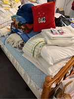 Stack of handmade crochet afghans, fleece throws, decorative pillow with snowman design, and folded bed linens on bed.