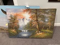 Two large unframed nature paintings on canvas depicting mountains, waterfalls and trees in warm autumn hues.