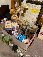 Top view of box containing bathroom items, plush bunny, and partially visible framed mirror behind